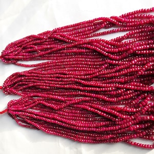 May include: A strand of deep red ruby beads, faceted and polished, with a knotted string at each end. The beads are arranged in multiple rows, creating a luxurious and elegant look.