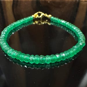 May include: A vibrant green gemstone bracelet with a gold clasp. The bracelet is made of small, faceted green beads strung together. The gold clasp adds a touch of elegance to the jewelry.