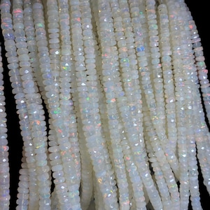 May include: Strands of white opal beads with a faceted cut. The beads have a subtle iridescence, displaying flashes of color. The beads are strung together, creating a cascading effect. The background is black.