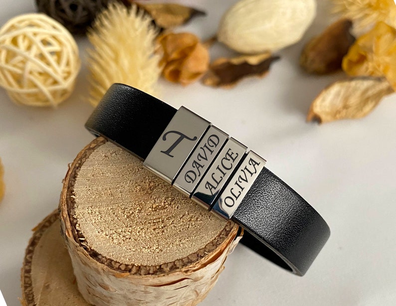 Puede incluir: Pulsera de cuero negro con abalorios de metal plateado grabados con los nombres "T", "David", "Alice" y "Olivia".