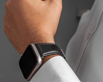 May include: A silver smartwatch with a black leather band on a person's wrist.