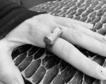 May include: A silver ring with a rectangular design. The ring is worn on a finger.
