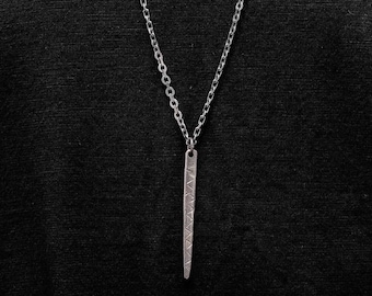 May include: A silver chain necklace with a long, thin pendant that has a geometric pattern.