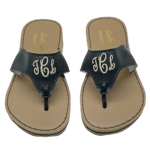 May include: A pair of navy blue flip-flops with a beige footbed and a black toe post. The straps feature embroidered initials in a cream color. The brand name "Southern Panama" is printed in gold on the side.