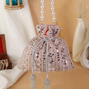 Puede incluir: Un bolso de mano rosa con cuentas, asa de perlas y borlas plateadas. El bolso está adornado con perlas y pequeños cuadrados espejados. El asa es de perlas blancas. El bolso es de forma pequeña y redonda.