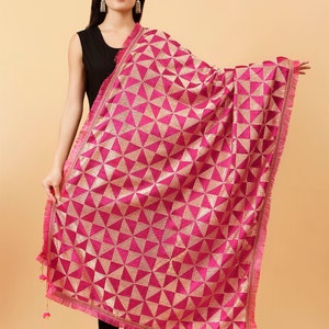 Może przedstawiać: R&oacute;żowo-złoty szal z frędzlami. Szal ma geometryczny wz&oacute;r z tr&oacute;jkątami i subtelnym połyskiem.