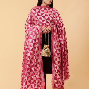 Może przedstawiać: R&oacute;żowo-złoty dupatta z frędzlami. Dupatta jest zarzucony na osobę ubraną na czarno.