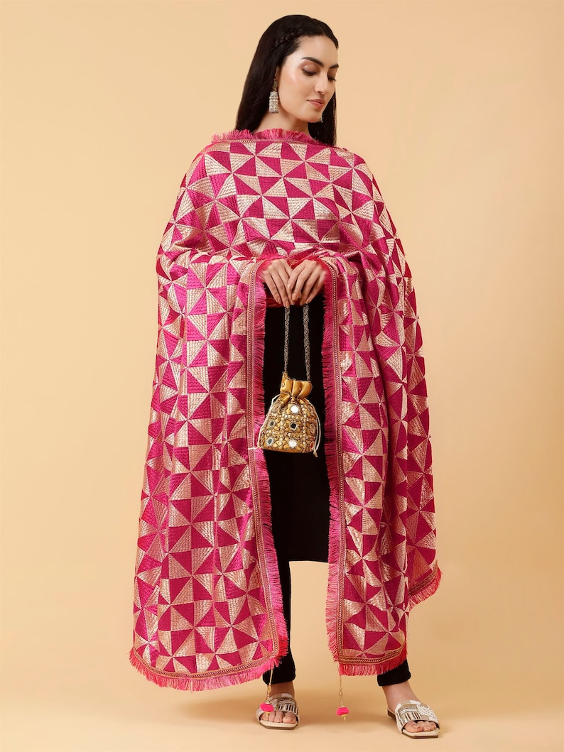 Może przedstawiać: R&oacute;żowo-złoty dupatta z frędzlami. Dupatta jest zarzucony na osobę ubraną na czarno.