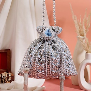 Puede incluir: Un bolso con cordón azul claro con cuentas y adornos plateados y blancos. El bolso tiene un asa con cuentas de perlas y borlas. El bolso está decorado con pequeños espejos y perlas.