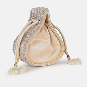 Könnte beinhalten: Eine cremefarbene Kordeltasche mit Perlenmuster und goldenen Quasten. Die Tasche ist aus einem weichen, samtigen Material gefertigt.