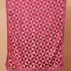 Może przedstawiać: R&oacute;żowy szal z aksamitu z geometrycznym wzorem złotych tr&oacute;jkąt&oacute;w. Szal ma frędzlową krawędź i frędzle.