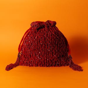 Może przedstawiać: Czerwona torebka ze sznurkiem i koralikami, z aksamitną górą i frędzlami. Torebka jest w głębokim czerwonym kolorze i pokryta małymi, odblaskowymi koralikami. Sznurek wykonany jest z pasującego czerwonego aksamitu.