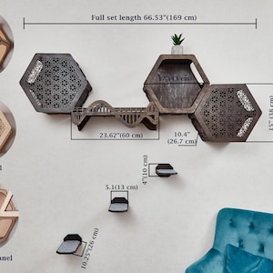 Puede incluir: Un &aacute;rbol para gatos de pared con estantes hexagonales y un puente. Los estantes son de madera y tienen un acabado natural. El puente es de madera y tiene un dise&ntilde;o ondulado. El &aacute;rbol para gatos mide 169 cm de largo. El &aacute;rbol para gatos se muestra con una peque&ntilde;a planta en uno de los estantes.
