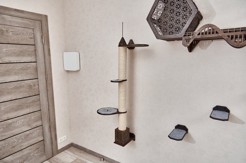 May include: A brown wooden cat tree with a scratching post and multiple platforms. The cat tree is mounted on a white wall. There are also several other cat shelves on the wall.