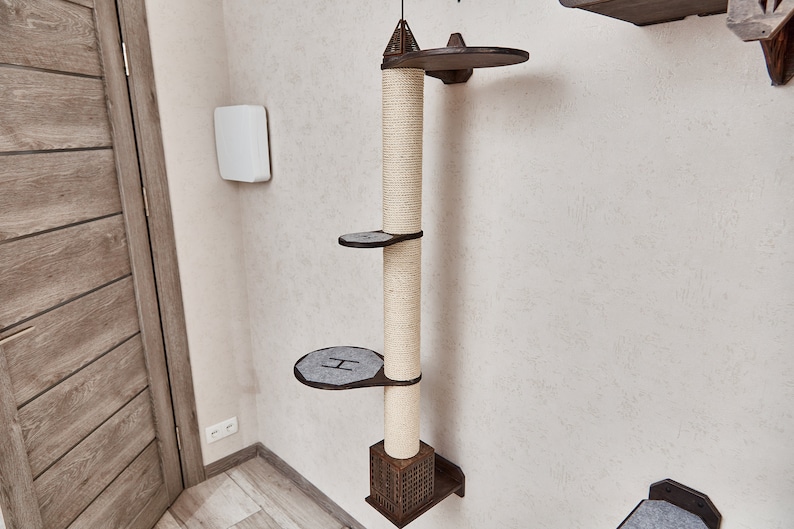 May include: A beige cat tree with a brown wooden base and three platforms. The cat tree is mounted on a white wall.