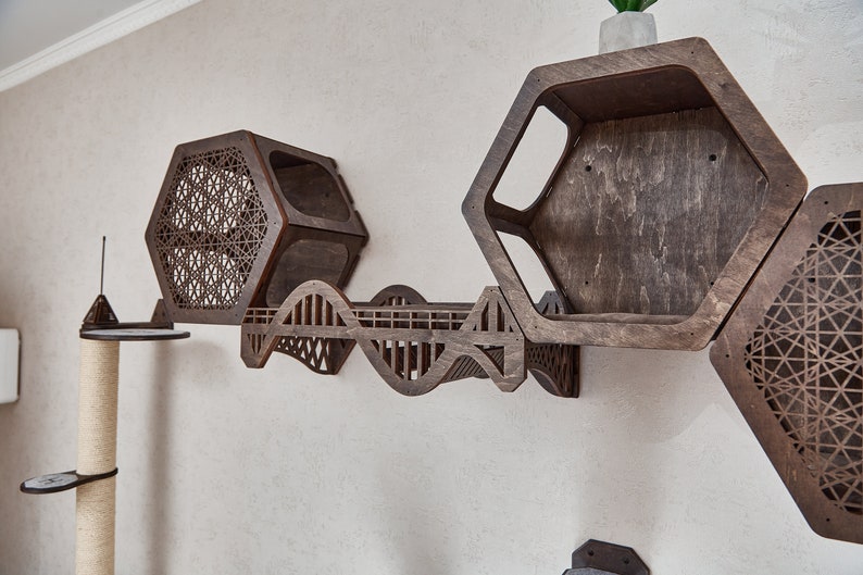 Puede incluir: Un &aacute;rbol para gatos de madera con un puente y varias estanter&iacute;as hexagonales. Las estanter&iacute;as tienen un patr&oacute;n geom&eacute;trico cortado en la madera. El &aacute;rbol para gatos est&aacute; montado en una pared.