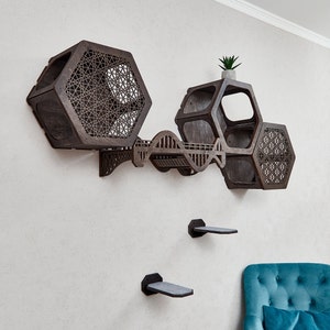 Puede incluir: Un &aacute;rbol para gatos de madera marr&oacute;n oscuro con un dise&ntilde;o hexagonal. El &aacute;rbol para gatos tiene varios niveles y una peque&ntilde;a planta en la parte superior. El &aacute;rbol para gatos est&aacute; montado en una pared blanca.