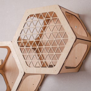 Puede incluir: Un conjunto de tres estantes hexagonales de madera con recortes geom&eacute;tricos. Los estantes est&aacute;n hechos de madera clara y est&aacute;n dise&ntilde;ados para montarse en una pared.