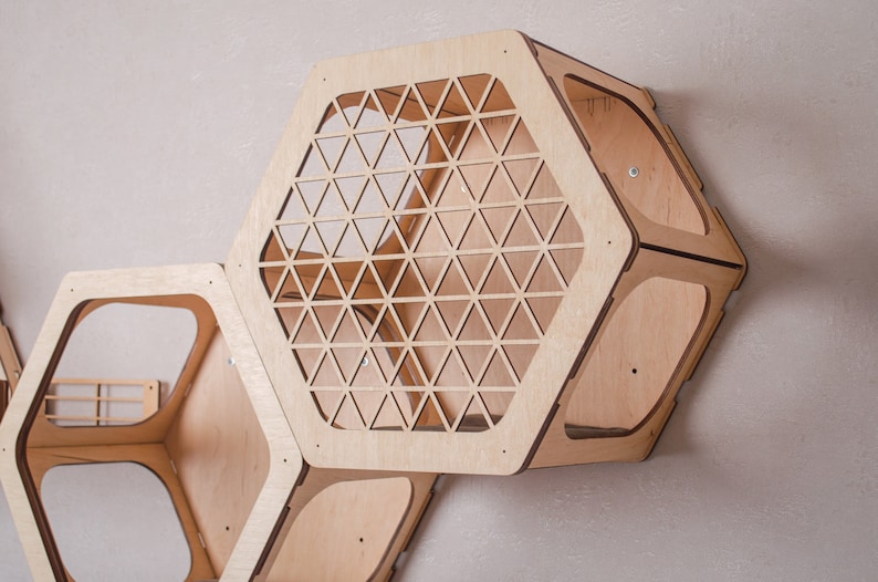 Puede incluir: Un conjunto de tres estantes hexagonales de madera con recortes geom&eacute;tricos. Los estantes est&aacute;n hechos de madera clara y est&aacute;n dise&ntilde;ados para montarse en una pared.
