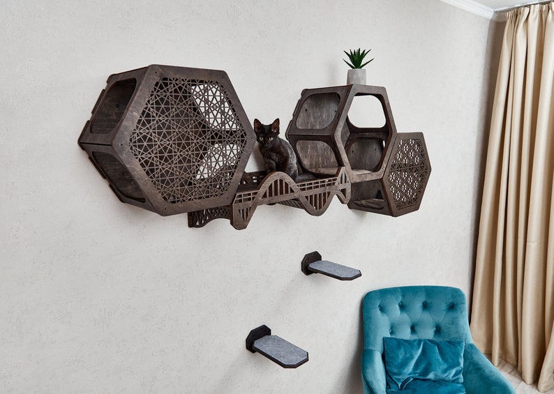 Puede incluir: Un &aacute;rbol para gatos de madera con m&uacute;ltiples niveles y un dise&ntilde;o hexagonal. El &aacute;rbol para gatos est&aacute; montado en una pared y tiene un gato negro sentado en uno de los niveles. El &aacute;rbol para gatos est&aacute; hecho de madera oscura y tiene un patr&oacute;n geom&eacute;trico.