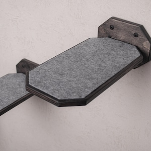 Puede incluir: Dos estantes grises para gatos con marcos de madera negra montados en una pared blanca. Los estantes est&aacute;n inclinados hacia arriba y tienen una superficie suave y texturizada.