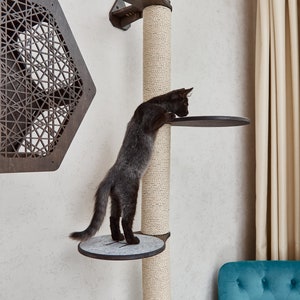 May include: A black cat climbing a sisal-covered scratching post with two platforms. The post is mounted to a white wall. The cat is looking down at the lower platform.