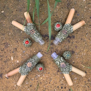 Peut inclure: Quatre flacons en céramique avec des motifs floraux verts et bruns et des bouchons en bambou. Chaque flacon a un petit couvercle rond rouge.