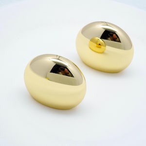 May include: Two gold-colored oval-shaped earrings. The earrings are smooth and shiny.