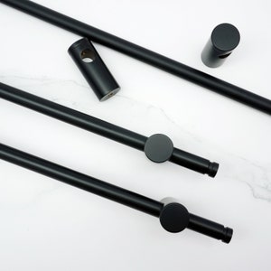 Puede incluir: Componentes negros de barra de ducha de metal, que incluyen varillas, conectores y una pieza cilíndrica. Las piezas están dispuestas sobre una superficie blanca, mostrando un diseño moderno y minimalista. Las varillas tienen un acabado mate.