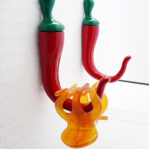 May include: Two red chili pepper shaped hooks with green tops. The hooks are mounted on a white wall.