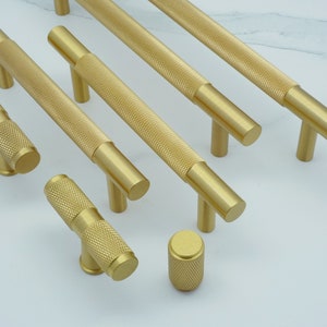 Può includere: Un set di pomelli e maniglie per armadi dorati con finitura testurizzata. I pomelli e le maniglie sono di diverse dimensioni e forme.