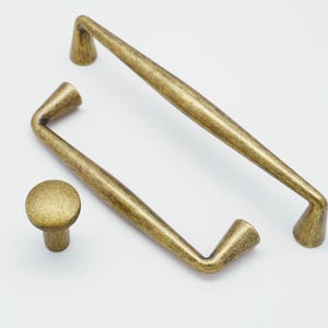 May include: Three antique gold cabinet pulls with a simple, elegant design. The pulls are made of metal and have a slightly distressed finish.