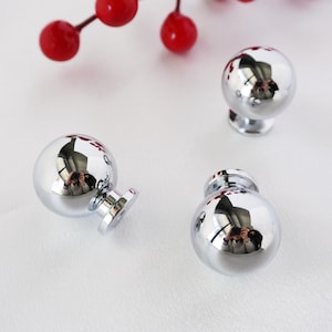 May include: Three silver round cabinet knobs with a shiny finish. The knobs have a round base and a round top.