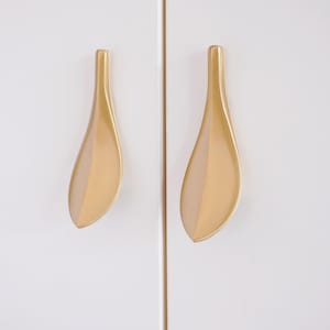 Peut inclure: Deux poignées de porte en forme de feuille dorées avec une finition lisse et brillante.