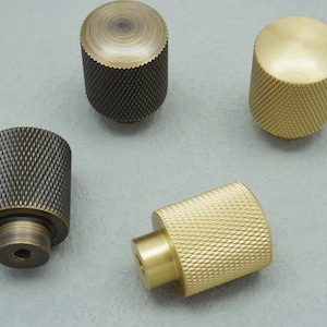 Könnte beinhalten: Vier Schrankknöpfe mit einem strukturierten Diamantenmuster. Zwei Knöpfe sind golden und zwei sind schwarz.