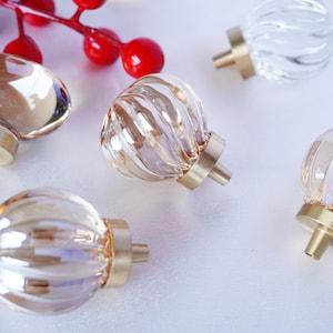 Puede incluir: Cinco pomos de armario de vidrio con bases de metal dorado. Los pomos son de varias formas, incluyendo redonda, ovalada y acanalada. Algunos pomos son de vidrio transparente, mientras que otros son de un color ámbar claro.