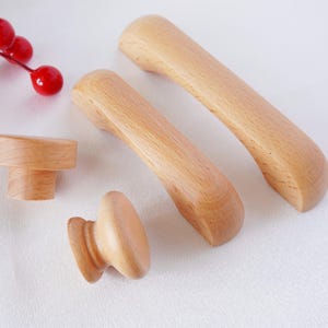 Puede incluir: Cuatro pomos y tiradores de armario de madera en varias formas y tamaños. Los pomos y tiradores están hechos de madera marrón claro y tienen un acabado liso.