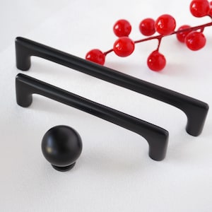 Peut inclure: Trois poignées de tiroir noires, deux sont longues et rectangulaires avec des bords arrondis, une est un bouton rond.