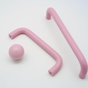 Op de afbeelding: Drie roze kastknoppen, twee zijn L-vormig afgerond en één is een bol.