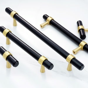 May include: Five black cabinet pulls with gold accents. The pulls are in various sizes and styles, including a long bar pull, a short bar pull, and a t-shaped pull.