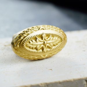 Peut inclure: Un objet décoratif doré de forme ovale, orné de motifs floraux et étoilés complexes. L'objet est très détaillé et semble être en métal. Le design est symétrique, avec une forme ovale centrale entourée de sculptures ornées.