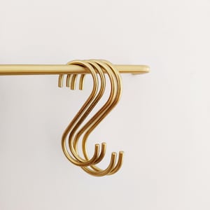 May include: Five gold-toned metal S-shaped hooks hanging from a gold-toned metal rod.