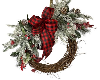 May include: A wintery wreath with a red and black buffalo plaid bow. The wreath is made of grapevine and is decorated with frosted pine branches, red berries, and pine cones.