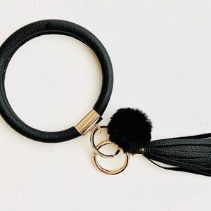 May include: Black leather key ring with a gold metal ring and a black faux fur pom-pom tassel.