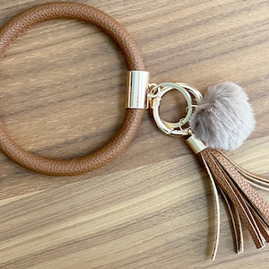 May include: A brown leather key chain with a gold ring and a fluffy gray pom-pom tassel.