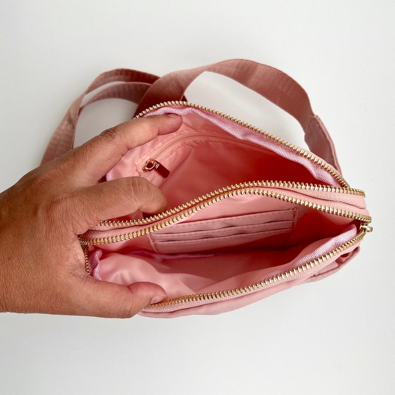 K&ouml;nnte beinhalten: Eine rosa Nylon-Umh&auml;ngetasche mit zwei Rei&szlig;verschlussf&auml;chern. Die Tasche ist offen und das Innere ist sichtbar.