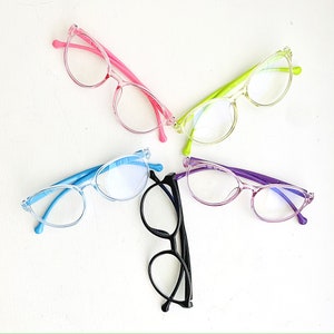 May include: Four pairs of eyeglasses with different colored frames: pink, green, blue, and purple. The glasses are all clear and have a rounded shape.