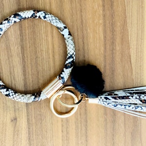 May include: A brown and white snake print key ring with a black fur pom pom and a matching tassel.