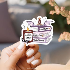 May include: A sticker featuring a stack of books with titles "Fated Mates", "Chosen One", and "Mystical Creatures". A candle with the text "smells like... FANTASY" is next to the books. A purple bat with a sword is above the books. The sticker has a purple butterfly and stars.