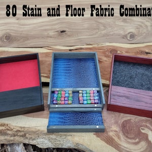 May include: Three wooden dice trays with different stain and fabric combinations. The tray on the left has a black stain and a red felt interior. The middle tray has a grey stain and a blue fabric interior. The tray on the right has a red stain and a black fabric interior. The middle tray is open and shows a collection of colourful dice.